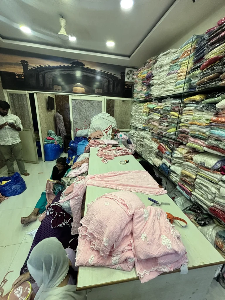 Shelves of folded Chikankari garments and a cutting table in the Smart Chikan Emporium stockroom